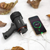 Black flashlight charging a smartphone on a white surface with leaves in the background